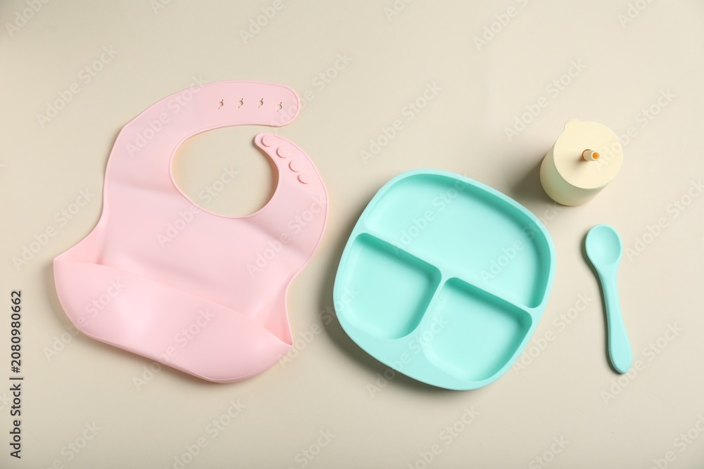 Obraz premium Set of baby tableware and silicone bib on beige background, flat lay
