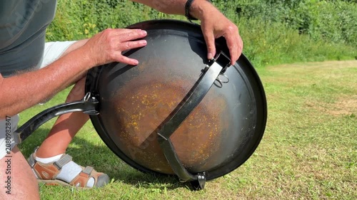 Close up of man hands unfolding and fixing metal legs on a portable camping fire pit.