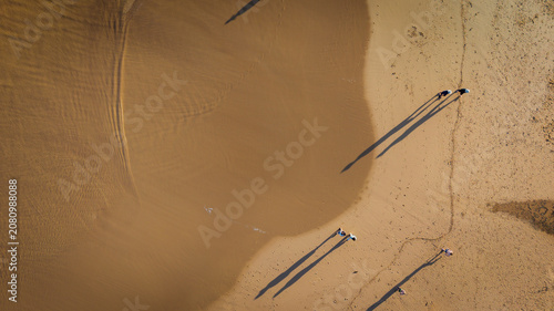 Aerial view of the sandy beach at Curl Curl with people walking along the shoreline casting long shadows on the sand in Dee Why, NSW, Australia.