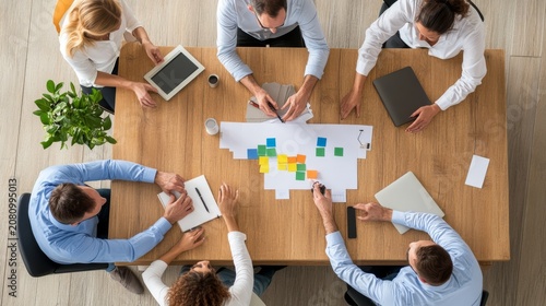Image content A high-angle (top-down) view of five professionals sitting around a wooden table in an office setting. Composition details Top-downaerial view, bird's eye view, central