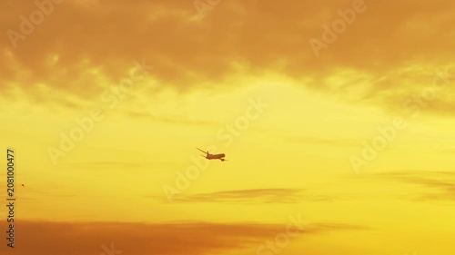 Passenger jet airliner flying through golden sunset sky filled with yellow orange clouds during evening golden hour, telephoto lens shot
