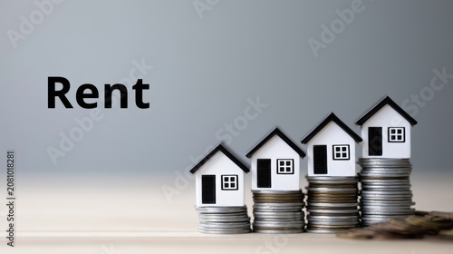 Miniature house models on growing stacks of coins representing rising rental prices