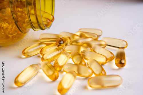 Yellow omega 3 fish oil capsules spilling out of a bottle on white background, top view.