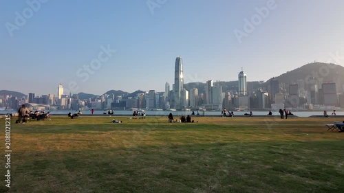 Time lapse shot, tourists and locals enjoying leisure time in the urban park of the West Kowloon Cultural District, with iconic Hong Kong Island skyline on background