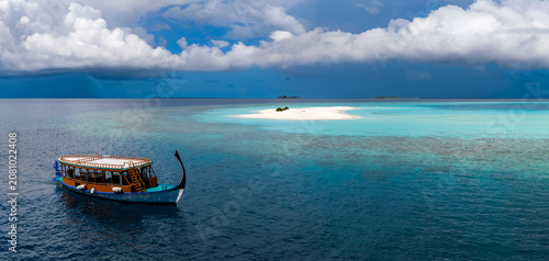 Tableau sur toile Aerial view shows a Maldivian dhoni drifting toward a tiny sandbank near Dhigurah Island, Maldives, over cobalt water and turquoise shallows under towering cumulus clouds