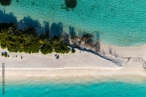 Aerial top down view of Dhigurah Island, Maldives, with a slender sandbar, white sand beach, coral shallows, deeper lagoon, rippling water, and midday light.