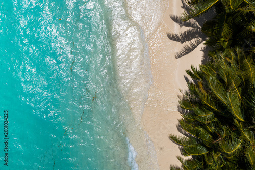 Fotografija Aerial midday view of Dhigurah Island, Maldives, where turquoise lagoon waves lap white sand, palm fronds cast feathery shadows, and gentle surf patterns shimmer in clear weather