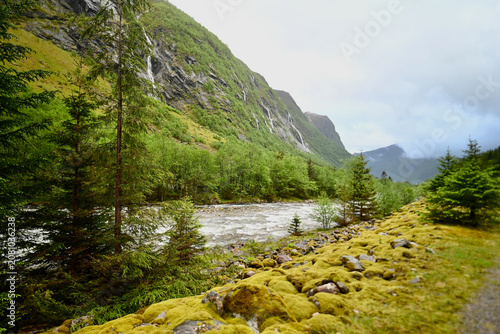 River valley near Dale, Norway, surrounded by cliffs, dense green forest, and moss-covered landscapes after rain on a cloudy late spring day.