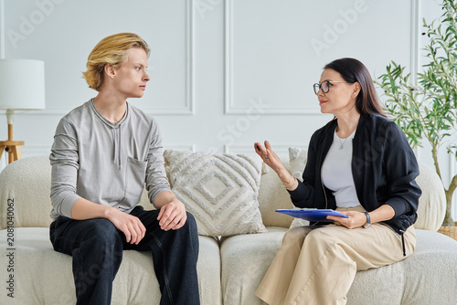 Female psychologist gesturing and talking to attentive teenage boy patient during therapy session