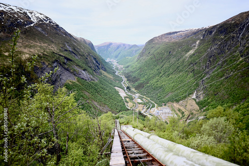 View from a staircase and industrial pipe down to the valley of Dale, Norway, on a sunny summer day with mountains and colorful Nordic scenery.