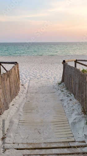Vertical POV walking through sandy dunes towards the beach at sunset with golden light and peaceful coastal landscape