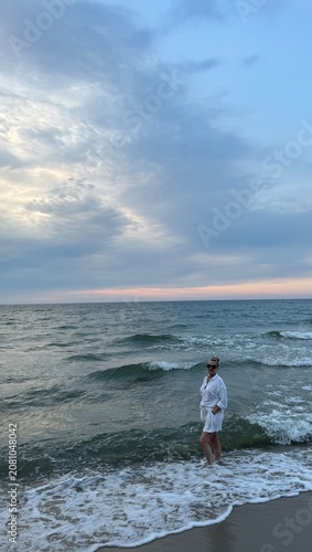 woman in sunglasses and a white suit stands on the seashore. The concept of recreation