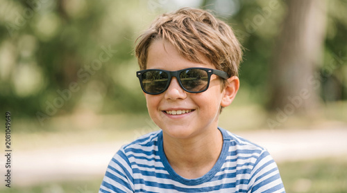 Happy boy wearing sunglasses and smiling in the park during daytime  