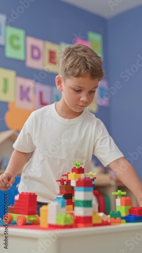 Boy stacking colorful blocks with his hands on a table amid alphabet cards in a school building; concentration creativity.
