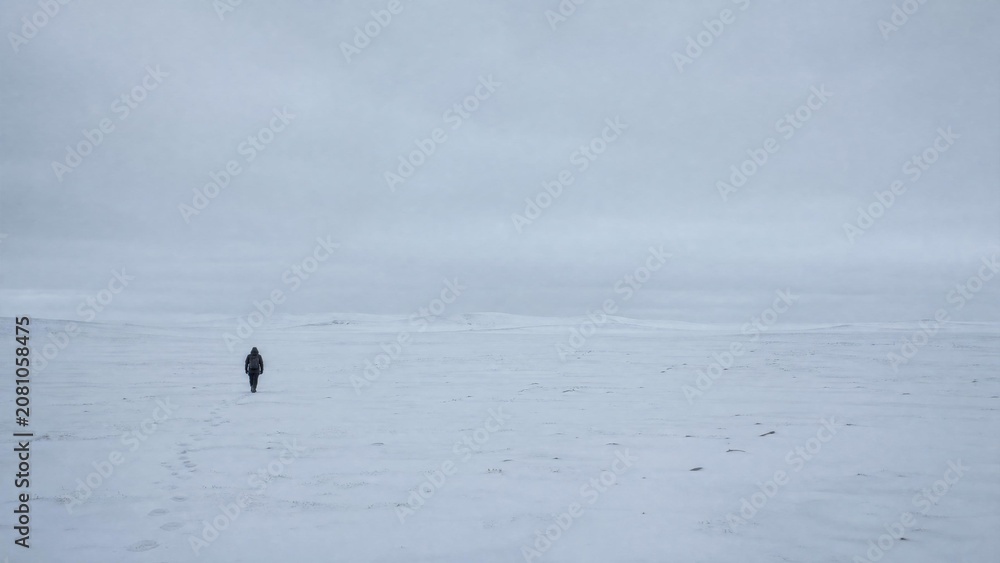 Fototapeta premium Solitary Hiker Walking Across Vast Arctic Tundra Snow Landscape