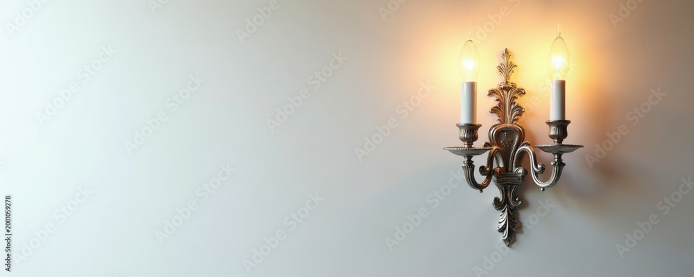 Obraz premium Antique silver wall sconce with two candle bulbs emits warm glow. Classic ornate design mounts on bright white wall. Adds elegance and vintage charm to interior spaces.