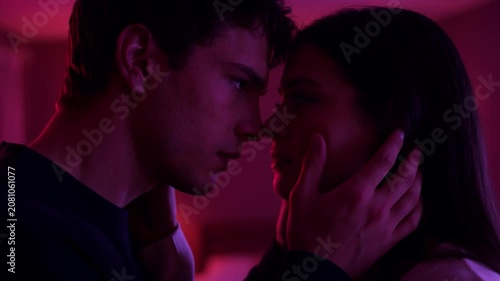 Passionate couple looking at each other before kissing in a purple neon light filled bedroom