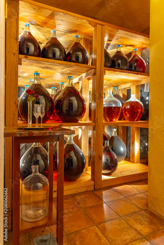 Fotografi Glass carboys filled with cider on wooden shelves in a cellar