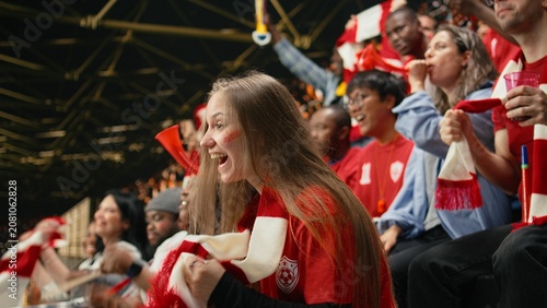 Foto Young female football supporter holding red scarf near her mouth, with face paint anxiously watching tense live soccer match from stadium stands, Women empowerment and football culture