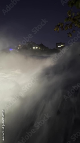 SCHAFFHAUSEN, SWITZERLAND - OCTOBER 11, 2025: Night view of the illuminated Rhine Falls with powerful cascading water and city lights surrounding the famous natural landmark.