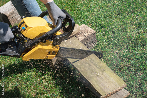 Canvas-taulu Man cutting wooden plank with chainsaw outdoors