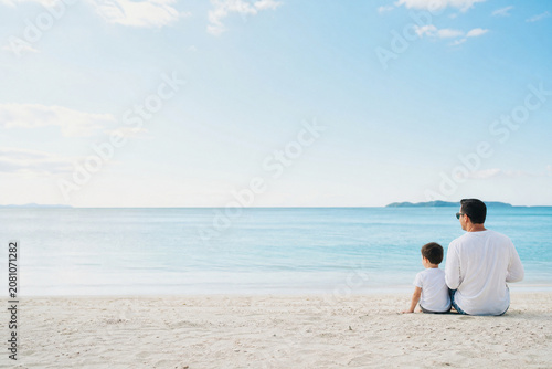 Pai e filho pequeno sentados na areia da praia olhando o mar com amplo espaço para texto - Conceito de serenidade, amor paterno e férias em família.
