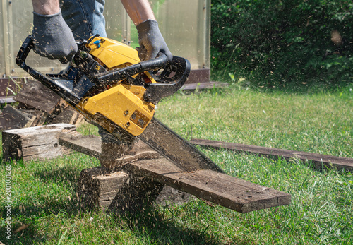 Valokuva Man sawing old wooden board with chainsaw outdoors