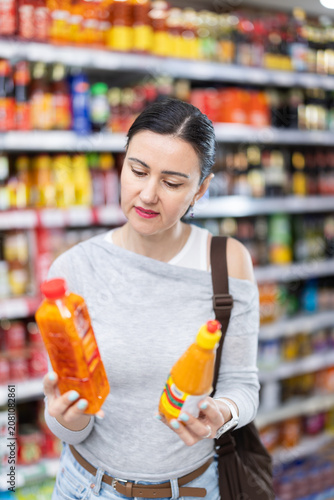 Woman buyer examines assortment, reads product label information before buy sauce. Client compares different options item, chooses product goods and check shelf life