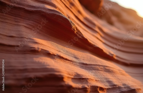 Close-up view of wavy red rock formations with layered patterns. Warm sunlight illuminates stone curves, highlighting natural erosion and fine granular texture in desert landscape.