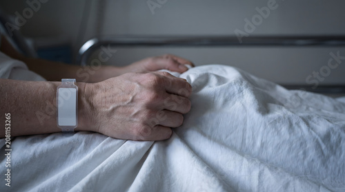 Old person hand resting on white hospital sheet depicting vulnerability medical neglect loneliness and health anxiety