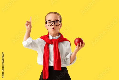 Billede på lærred Little schoolgirl with apple pointing at something on yellow background