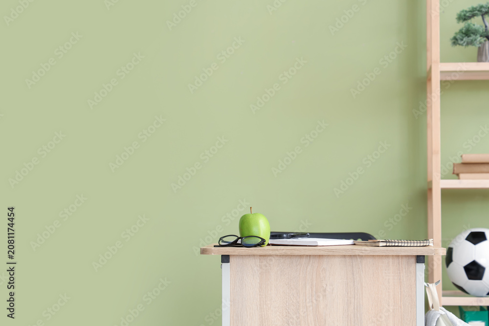 Fototapeta premium Apple with eyeglasses on desk near green wall in classroom