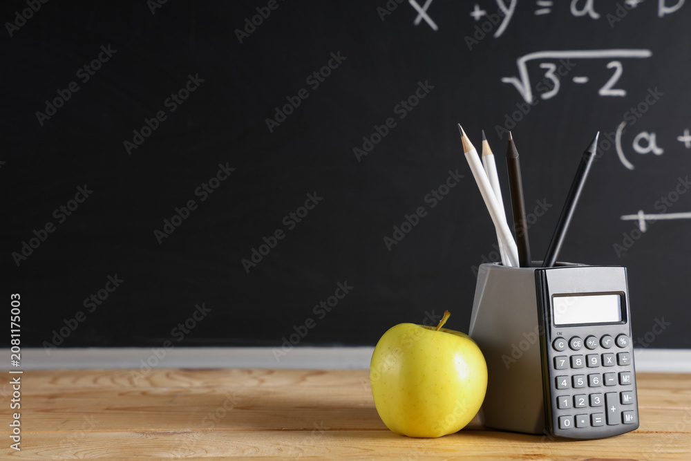 Obraz premium Apple, calculator and pencils on desk near chalkboard with formulas. Back to school concept