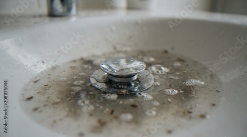 Schilderij op canvas A close-up view of a clogged bathroom sink filled with murky, stagnant water and debris around the metal drain