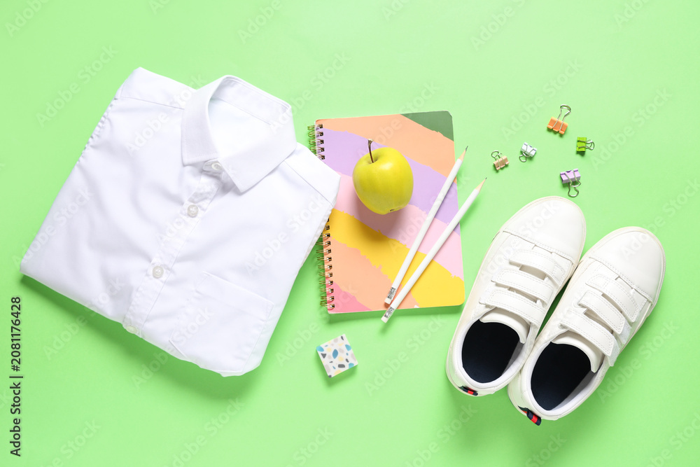 Fototapeta premium Tasty apple, shirt, shoes and different school stationery on green background