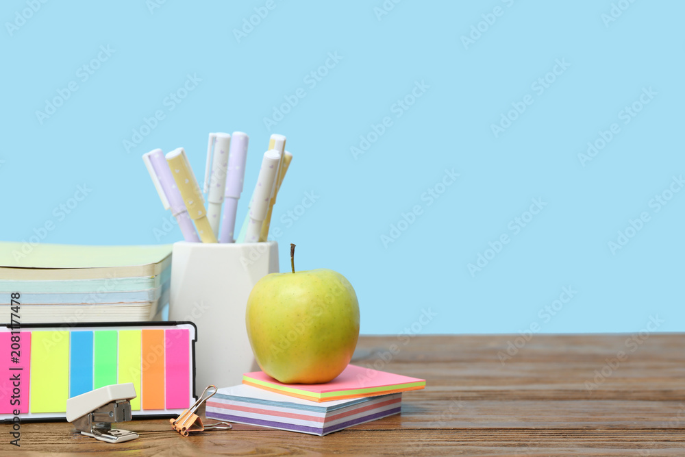 Obraz premium Pencil holder, sticky notes, different school supplies and green apple on table against blue background