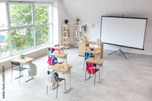 Blurred view of light classroom with projector screen and desks