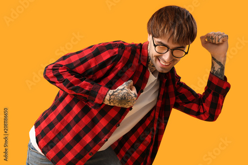 Young tattooed man dancing against yellow background