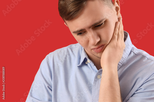Young man suffering from toothache on red background, closeup