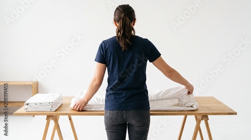 Photorealistic person viewed from behind, no face, folding fitted sheets, fabric handling, clean white isolated backdrop