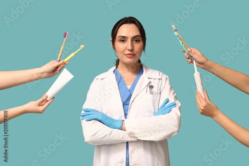 Young female dentist and hands holding toothbrushes on blue background