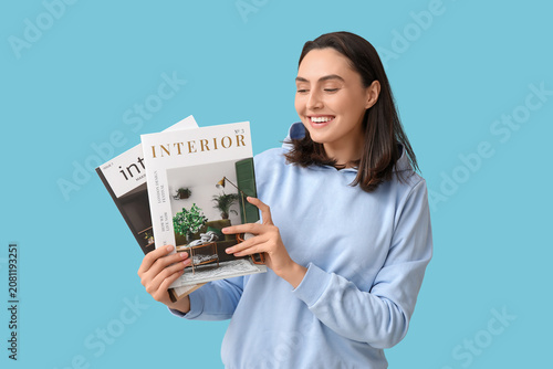 Beautiful young woman with interior magazines on blue background