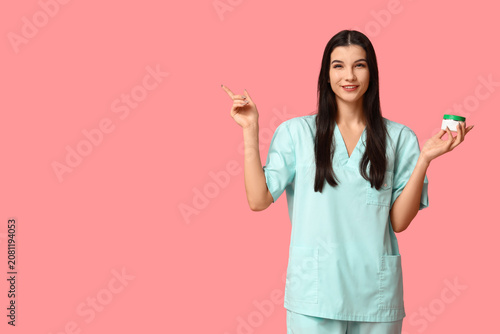 Tableau sur toile Beautiful young happy female beautician with jar of cream pointing at something