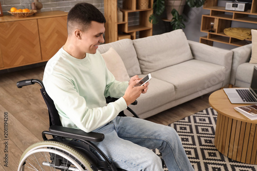 Happy young man in wheelchair using mobile phone at home