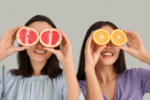 Beautiful young women with fresh grapefruit and orange on grey background