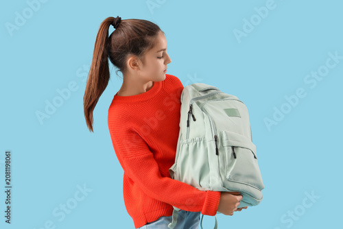 Little schoolgirl with backpack on blue background