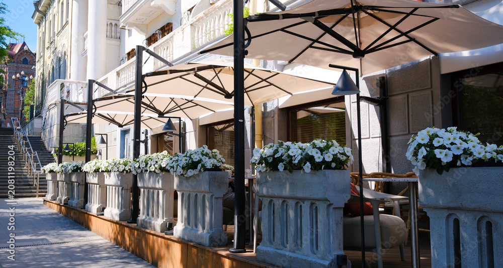 Obraz premium A summer street scene with a charming street cafe featuring a row of tables and chairs, inviting passersby to immerse themselves in the cafe's urban culture.
