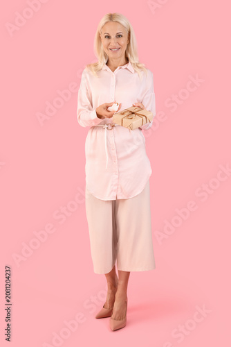 Obraz na plátně Mature woman with gift and vibrator on pink background