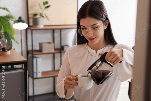 Young businesswoman pouring coffee into cup in office