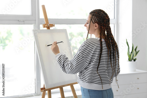 Young woman with dreadlocks painting on easel at home